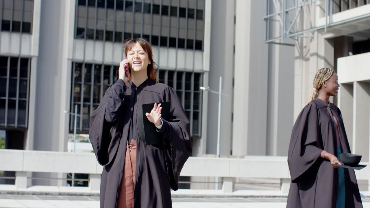 Donna asiatica di mezza età in toga per la laurea che parla al telefono mentre un collega esce dalla piazza, spazio libero