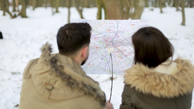 Un couple caucasien consultant une carte dans une forêt enneigée.