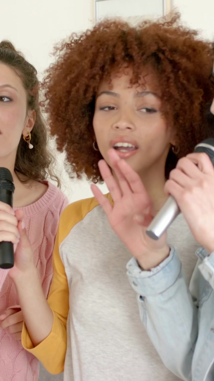 Video verticale: Donna a destra che canta e inizia una canzone, amici che si scambiano i microfoni sul divano per divertimento, in jeans