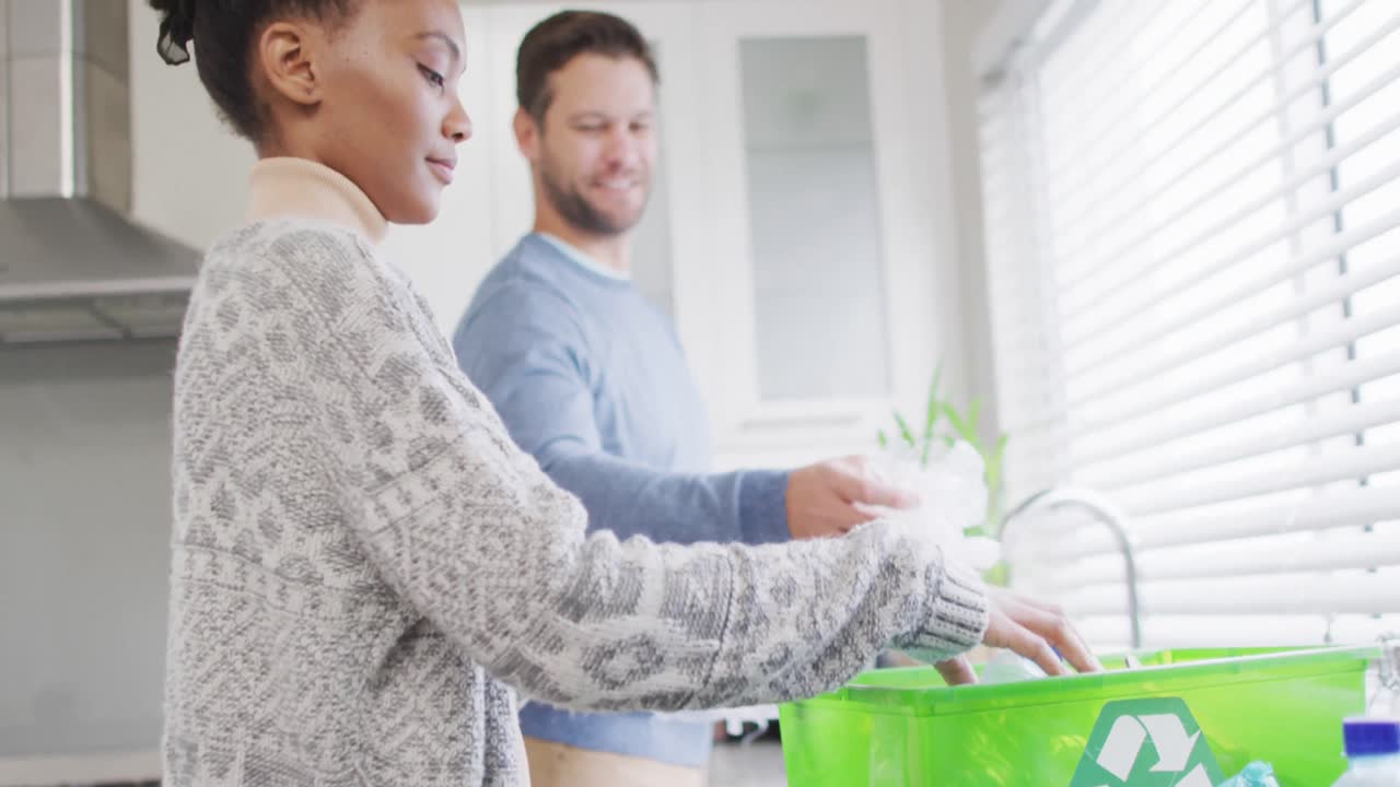 Video of happy diverse couple collecting plastic bottles for recycling at home