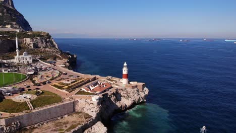 Faro-De-Rayas-Rojas-Y-Blancas-Y-Una-Gran-Mezquita-En-Europa-Point-En-Gibraltar-Con-Vistas-A-Varios-Cargueros-Anclados-Mientras-El-Oleaje-Mediterráneo-Salpica-Contra-Los-Acantilados