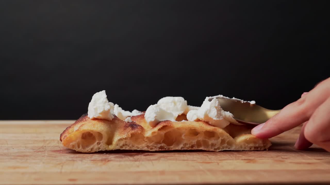 Spoon places fresh cheese on pizza dough in slow motion, studio black background