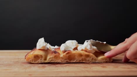 un cucchiaio mette formaggio fresco sull'impasto di pizza al rallentatore, sfondo nero in studio