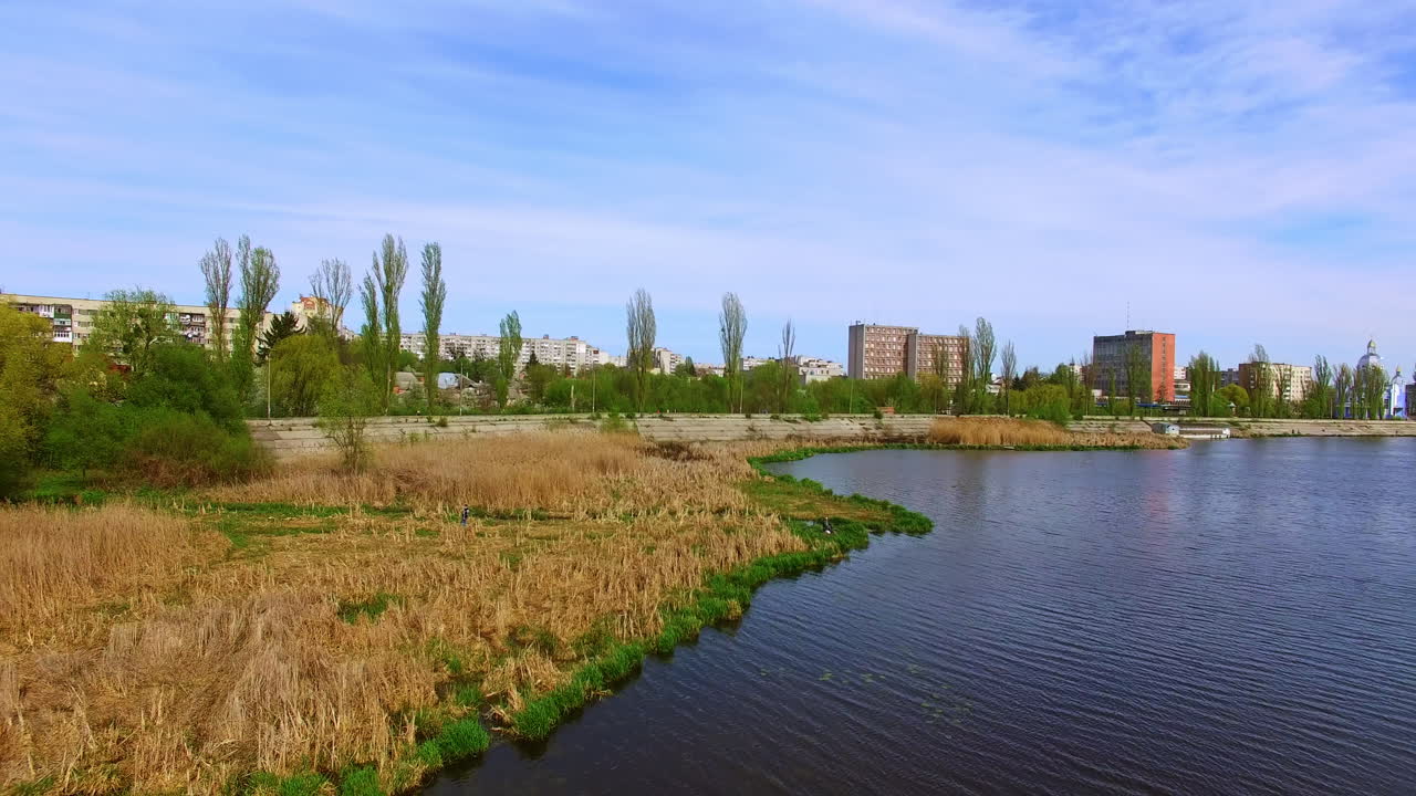Dry reed growing on the river bank. City view with high-rise multi-storied buildings at backdrop.