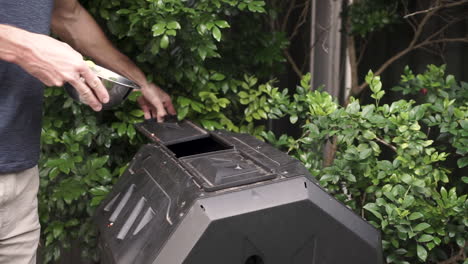 el hombre caucásico pone los desechos de alimentos en el contenedor de compost del patio trasero, tiro medio fijo