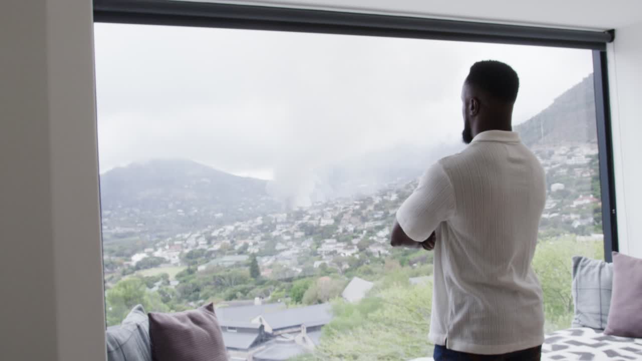 African adult man standing right at window, responding to valley plume smoke and mist, copy space