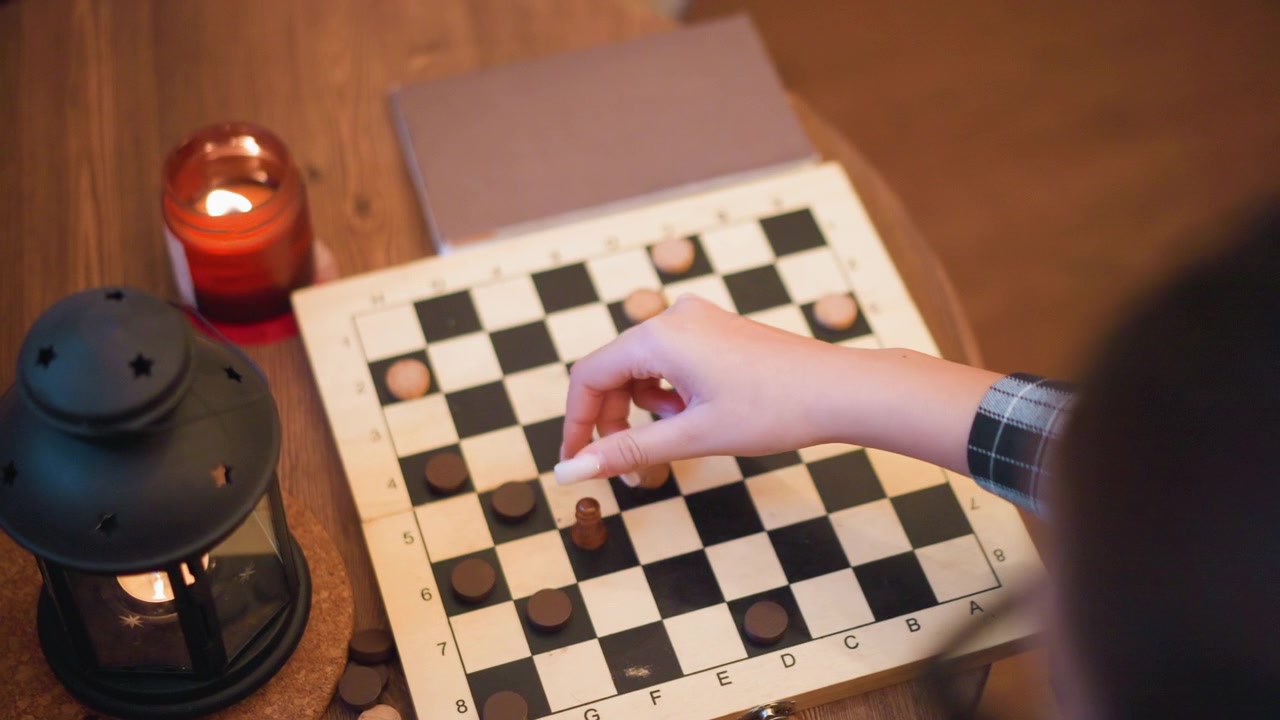 Jovem mulher joga damas em uma mesa de madeira, movendo as peças pelo tabuleiro. A cena inclui iluminação quente de velas e lanternas, com close-ups de sua mão com as fichas do jogo.