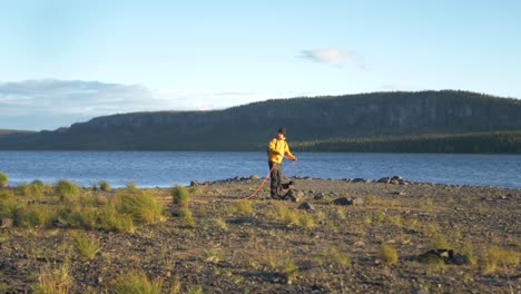 lappland lake side view with camper man tying rope around large rock - wide push in slow motion shot