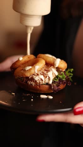 preparing a delicious burger with onion rings and creamy sauce