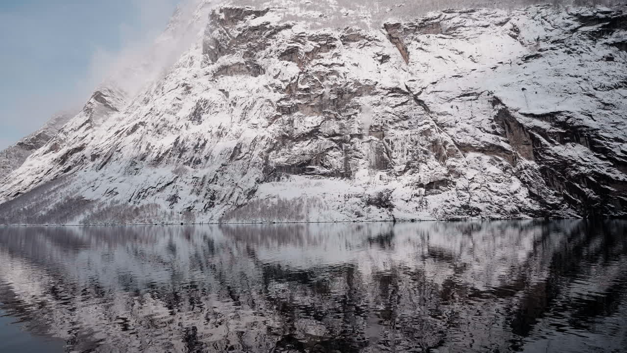 Zeitlupen-POV einer winterlichen Fährfahrt im Geirangerfjord nach Geiranger, Norwegen, mit verschneiten Bergen und faszinierenden Fjordblicken