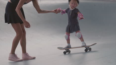 mother helping little daughter skateboarding