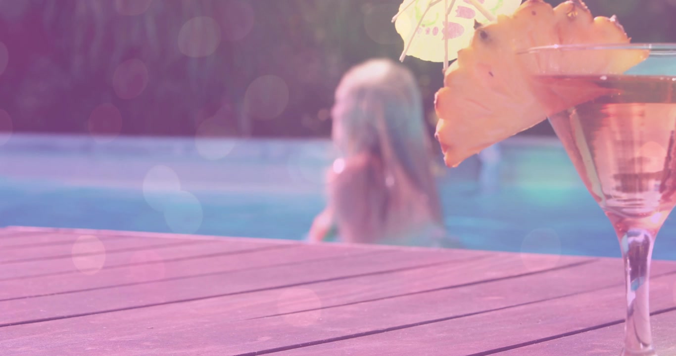Sunlit pool deck featuring cocktail glass, woman lifting head and pushing arms, creating ripples
