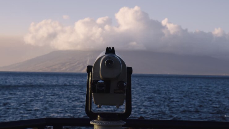 Telescopio puntato verso la Baia di Wailea e le Montagne di West Maui coperte di nuvole a Maui, Hawaii.