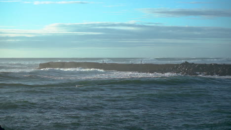 Two-foolish-people-on-a-jetty-in-Bandon-Oregon-during-strong-wind-and-waves,-ignorant-about-the-dangers