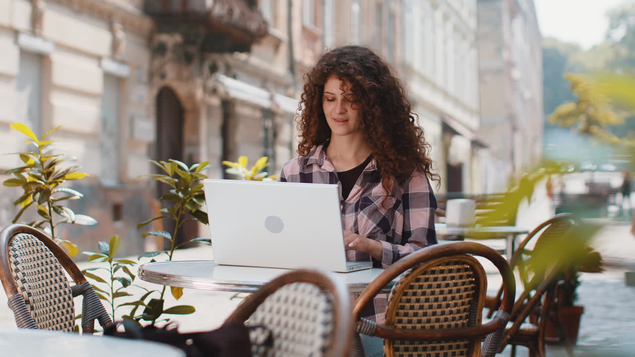 Woman working online distant job with laptop in city cafe or restaurant browsing website chatting
