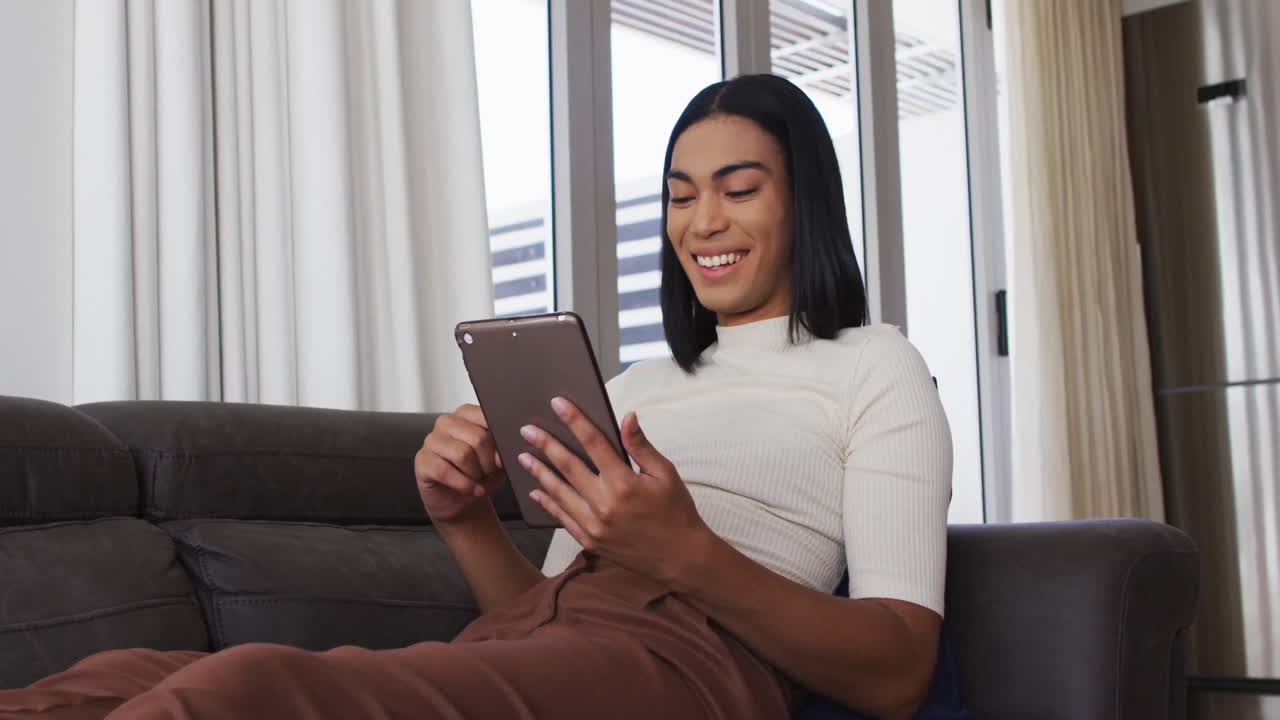 Mixed race gender fluid person sitting on couch and using tablet at home