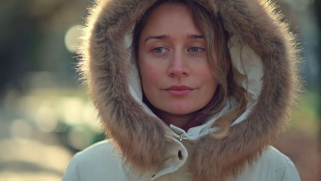 A woman wearing a warm white coat with a fur-lined hood walks through a park on a crisp winter day. She enjoys the serene atmosphere while taking in the beauty around her