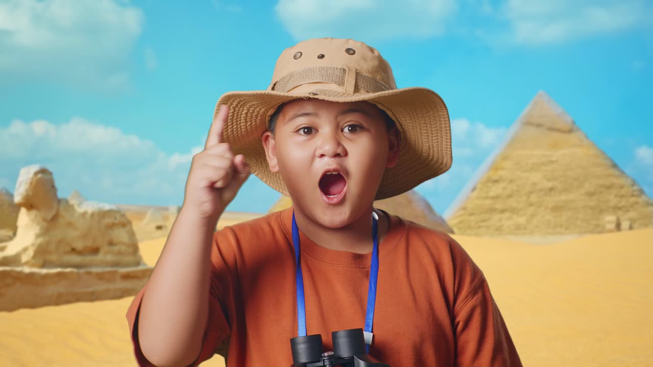 Asian Boy With A Hat And Binoculars Thinking And Looking Around Then Raising His Index Finger While Traveling In Giza Pyramid. Boy Researcher, Travel Adventure Concept, Close Up