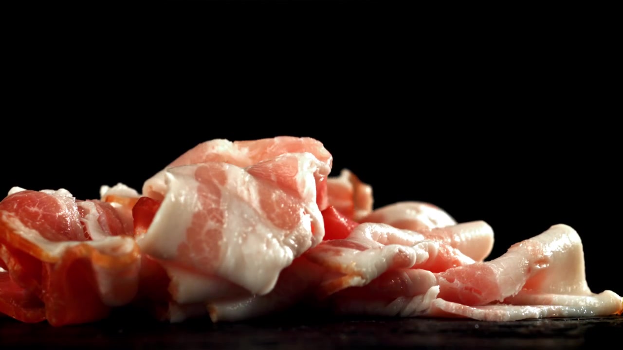 Fette di pancetta cruda che cadono al rallentatore su sfondo nero