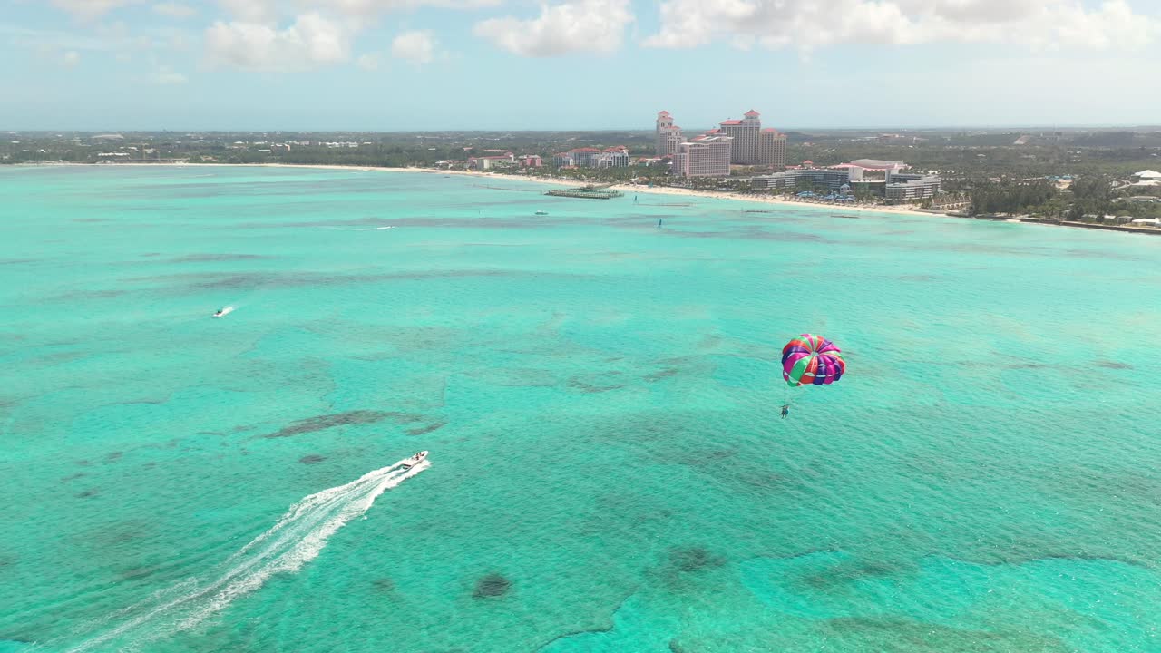 Parasailing in Bahamas, Drone Aerial View of Parachute Above Emerald Ocean Water and Beach Waterfront