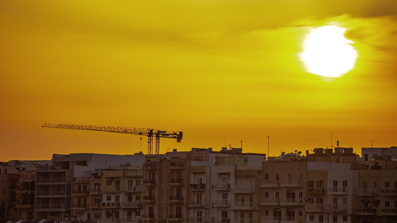 Sol brilhante se pondo atrás dos telhados de uma vila maltesa, vista em lapso de tempo