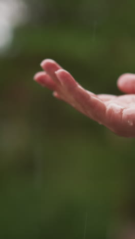 woman holds open palm in raindrops outdoors closeup. lady enjoys warm raindrop in park at spring downpour. living in harmony with nature concept