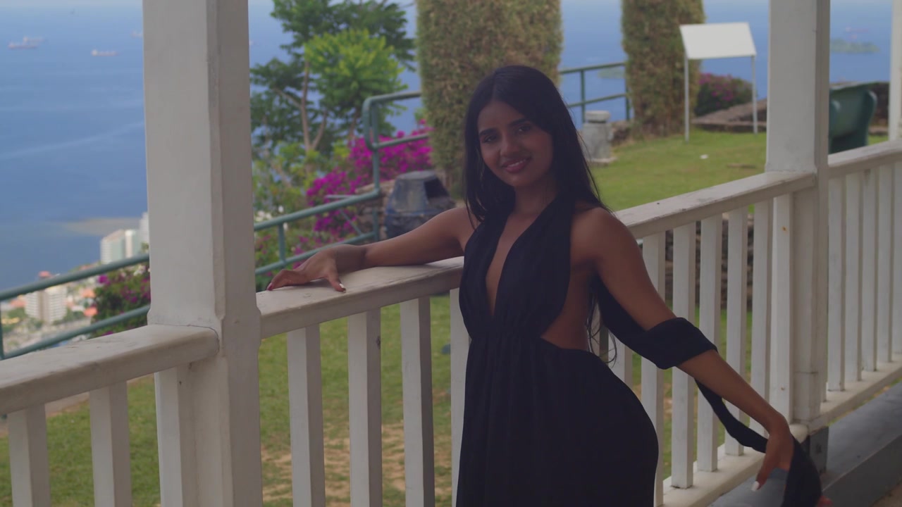Garota indiana com vestido preto em pé em um forte com vista para uma paisagem urbana ensolarada.