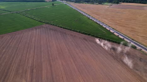 El-Tractor-Ara-El-Campo-De-Tierra-Hasta-El-Borde-En-ángulo-Con-Una-Nube-De-Polvo-Elevándose-Detrás-En-Un-Campo-Exuberante