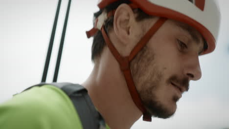 un joven excursionista con un casco blanco y naranja, pasando la cámara, bastones de senderismo puestos en la mochila