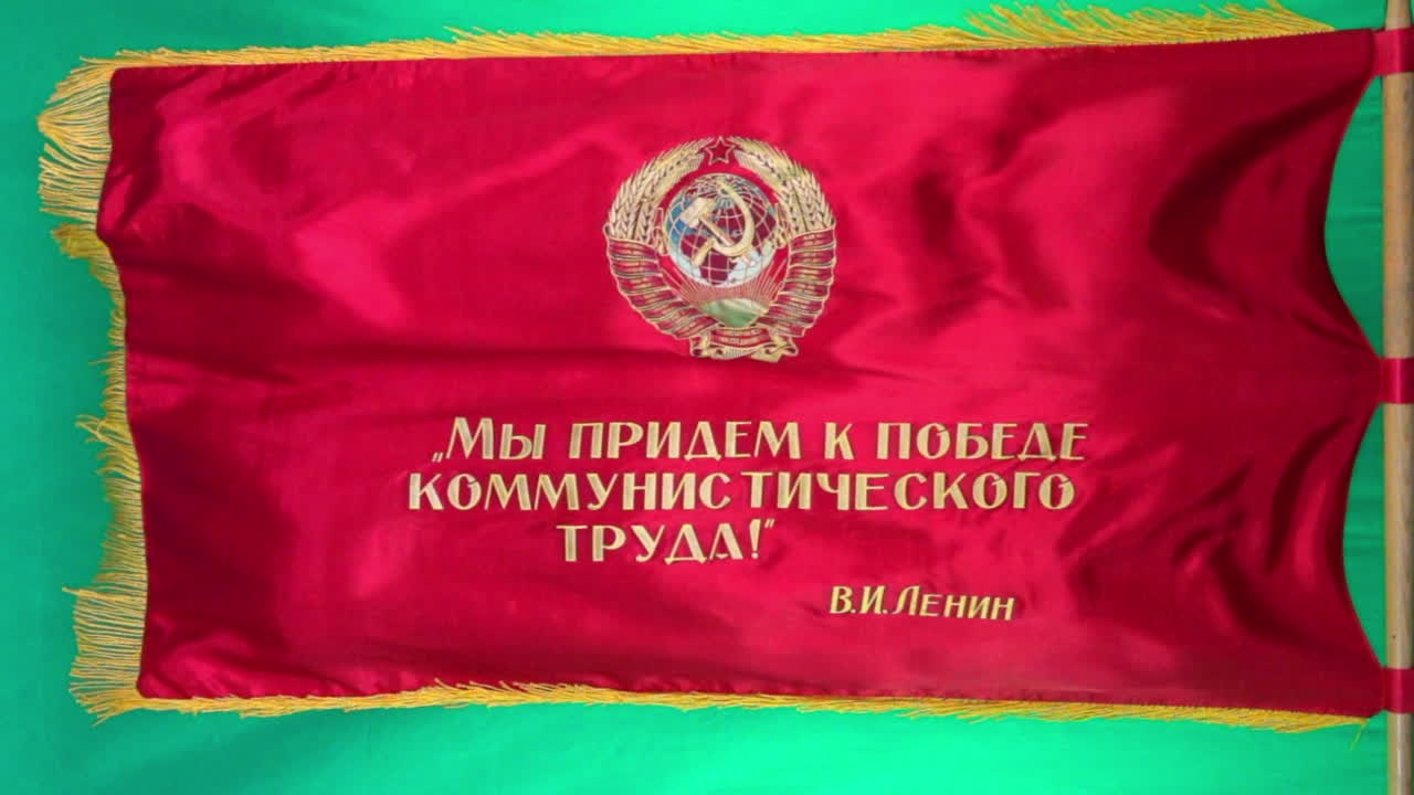 una bandera de desfile soviética que muestra un emblema de martillo y hoz vuela en cámara lenta contra un fondo de pantalla verde