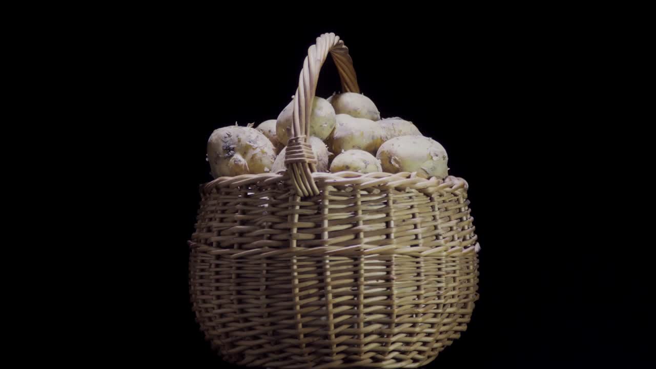 Composition of vegetables, rotation of a basket with root vegetables, potatoes, on a black background