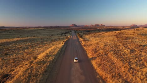 aerial view of a white car driving through a sunlit prairie landscape in namibia