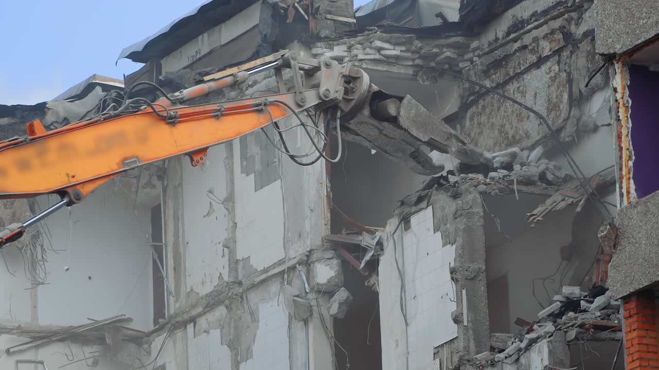 Breaking concrete walls and floors with the help of machinery. Dusty area of destruction site. Powerful claw ruins the house. View from below.