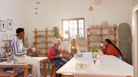 happy diverse group of potters drinking coffee and discussing in pottery studio