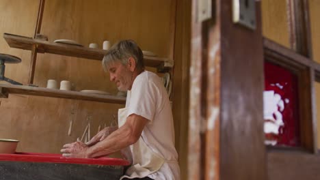 senior caucasian man wearing apron making pottery in his workshop