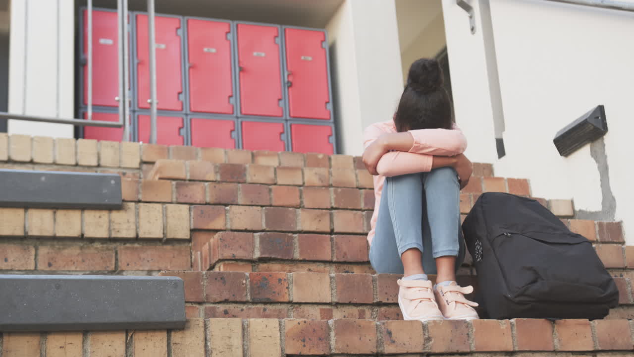 Sitting on school steps, African American girl with backpack feeling sad and alone, copy space