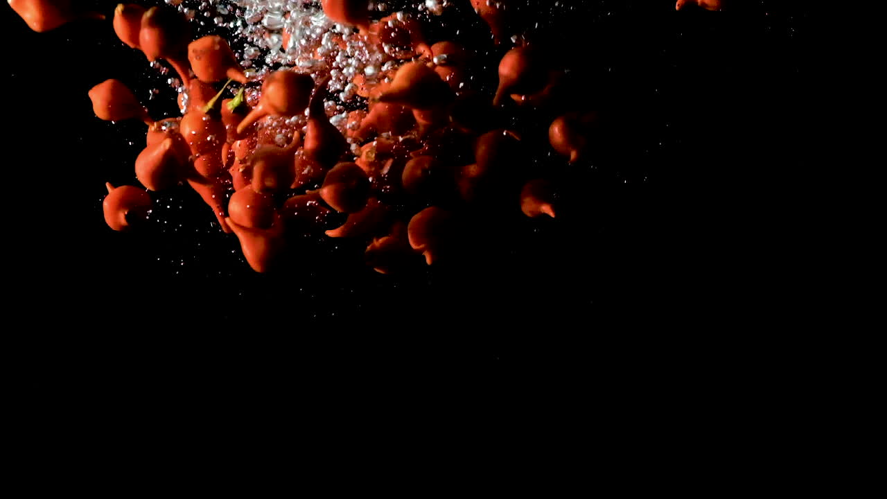 pimientos de pico caídos en agua sobre fondo negro, cámara lenta de cerca