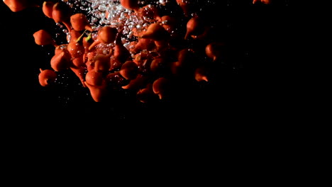 beak peppers dropped into water on black background, slow motion close up