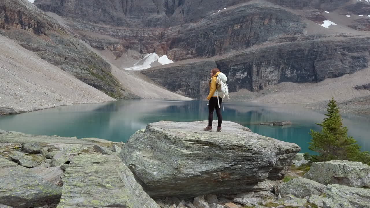 una mujer excursionista se encuentra en una enorme roca contemplando los majestuosos reflejos del lago oesa, alberta, canadá
