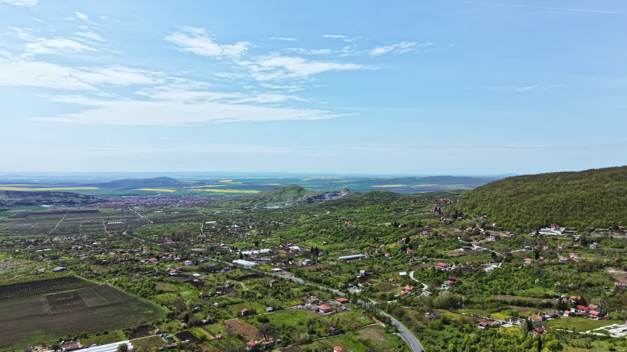 View of a rural landscape featuring fields, hills, and houses along a winding road near a body of water in a clear sky