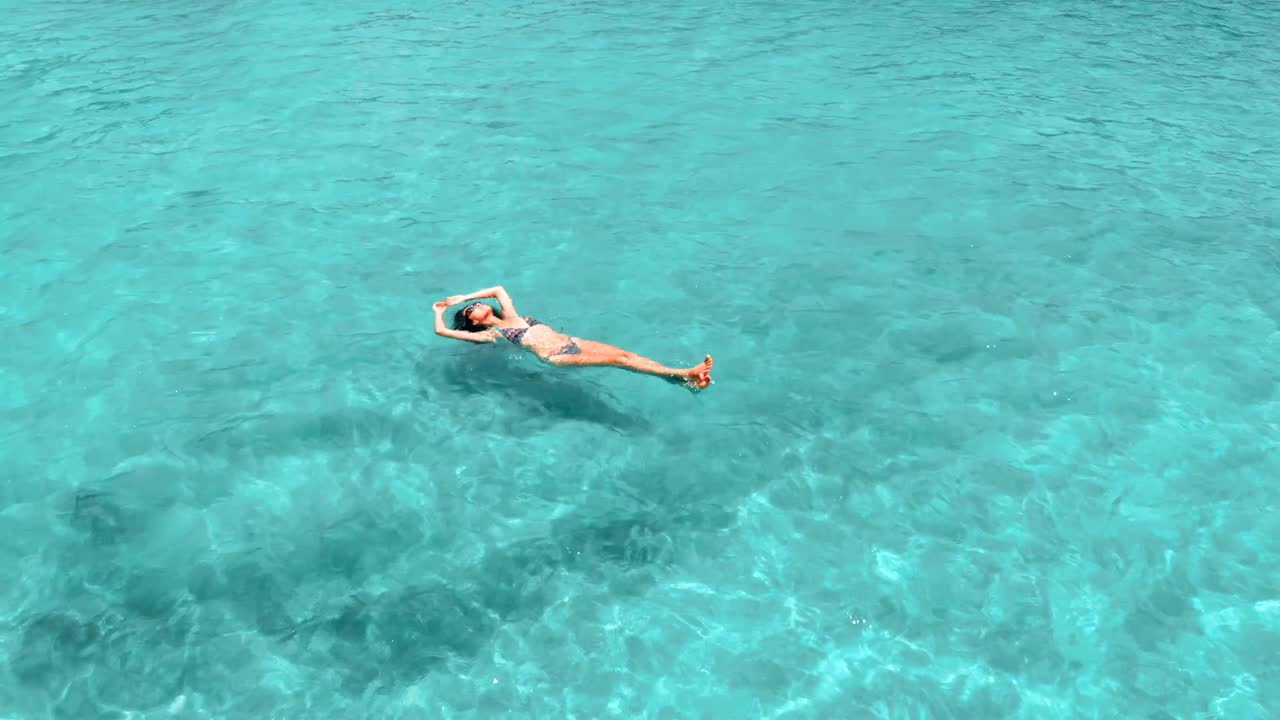 Beautiful young woman floating in crystal clear water, aerial rotating shot