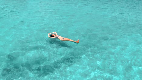 hermosa mujer joven flotando en agua cristalina, tiro rotativo aéreo