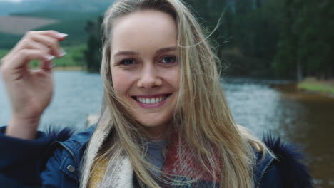 portrait-beautiful-blonde-woman-smiling-feeling-happy-enjoying-cold-winter-outdoors-by-lake-with-wind-blowing-hair-4k