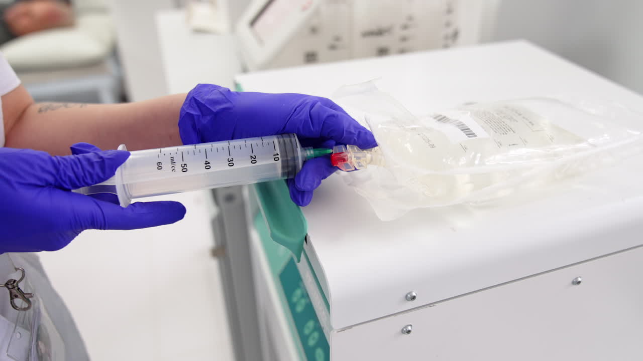 Unrecognized female medic holds a large syringe attaching it to the plastic bag. Preparation for prp-therapy. Close up.