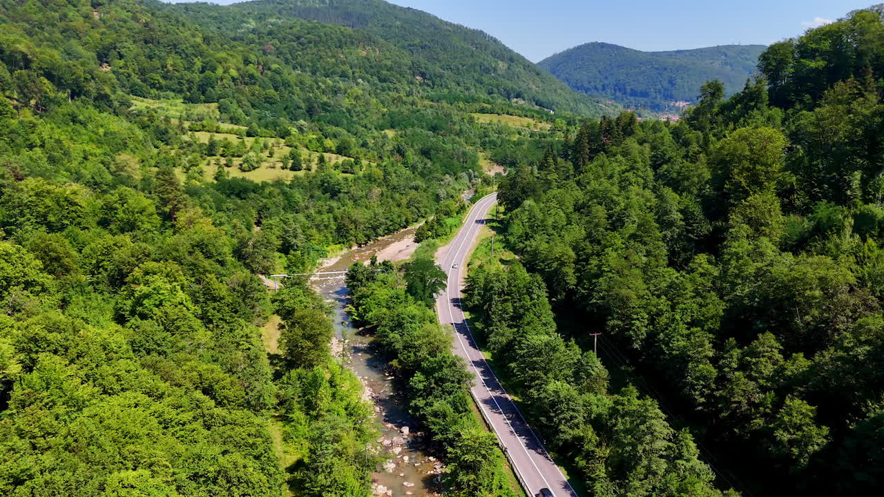 Winding river scenic highway. Lush green forests line a winding road next to a clear river during a sunny day in the countryside
