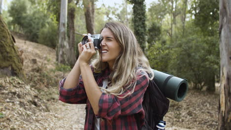 chica turista activa con cámara fotográfica tomando fotos del bosque