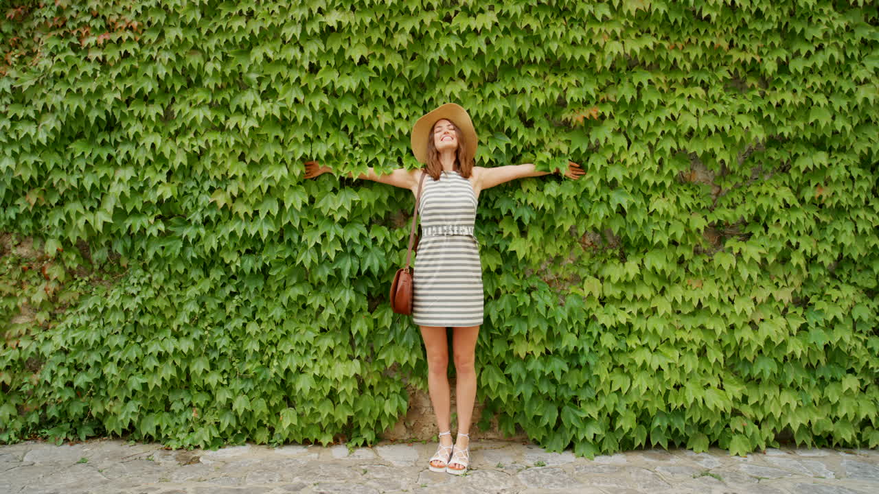 Donna in abito in posa davanti a un muro coperto d'edera