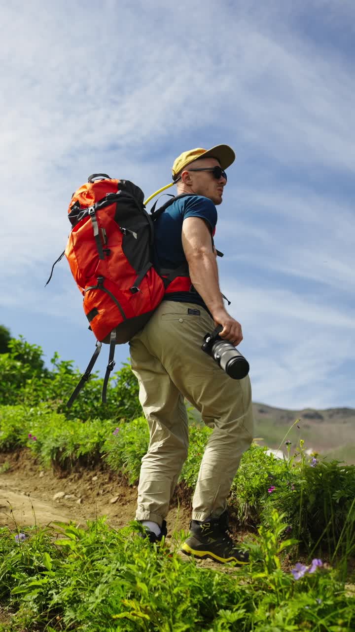 Escursionista con zaino e macchina fotografica in piedi su un sentiero di montagna verde