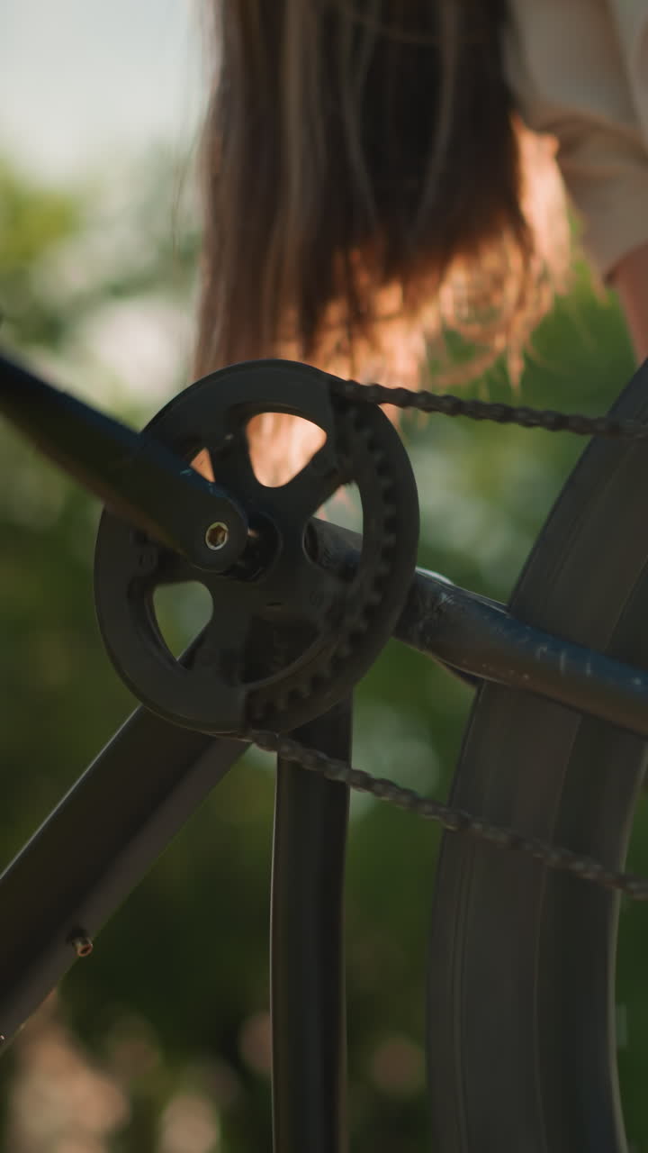 primer plano de una mujer inclinándose para girar el pedal de la bicicleta con la mano, haciendo que el neumático trasero gire, destacando el movimiento y la mecánica del ciclismo, el fondo incluye follaje verde