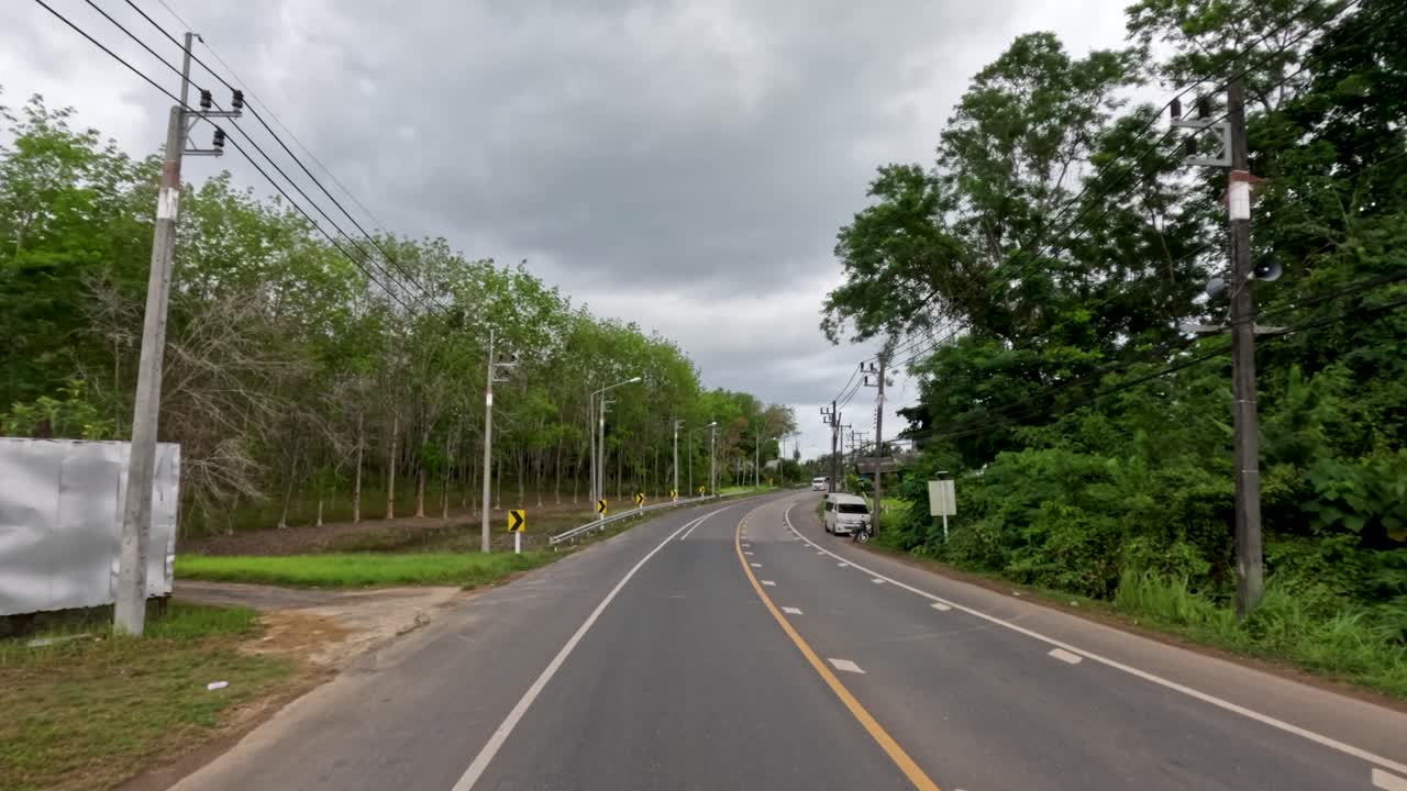 White van travels along winding rural asphalt road, lush tropical greenery, overcast daylight, steady camera